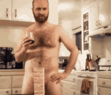 a naked man in a kitchen holding a glass of wine .