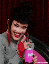 a woman with red hair and black nails is drinking from a pink can