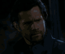 a man with a beard wearing a blue jacket looks down with his eyes closed