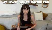 a woman sits on a couch playing an ukulele with at least you 're having fun written above her