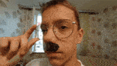 a young man wearing glasses holds a piece of black tape over his nose
