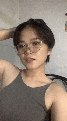 a woman wearing glasses and a grey tank top looks at the camera