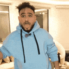 a man with a beard is wearing a light blue hoodie and making a funny face