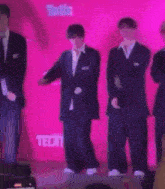 a group of men in suits are dancing on a stage in front of a pink wall that says tecate .