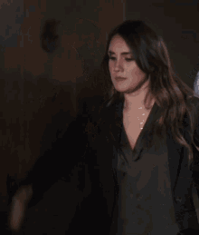 a woman wearing a black jacket and a green top stands in a dark room