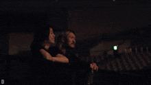 a man and a woman are sitting on a balcony at night with the letter d in the lower right corner