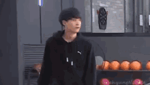 a young man in a black puma hoodie is standing in front of a dart board