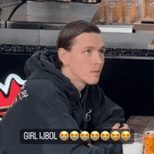 a man in a black hoodie is sitting at a table with a sign that says girl ijbol