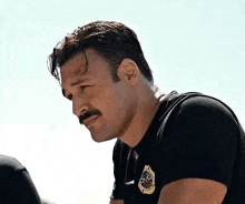 a man with a mustache is wearing a black shirt and looking down at something .