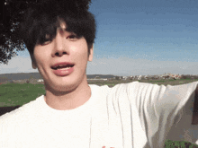 a young man wearing a white t-shirt is standing in a field with his mouth open