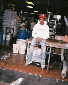 a man wearing a white hoodie that says fourup sits on a table in a kitchen