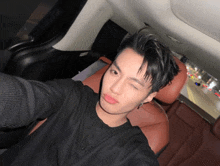 a young man in a black shirt is taking a selfie in a car