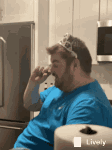 a man with a crown on his head is sitting in a kitchen next to a roll of paper towels that says lively