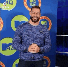 a man with a beard is smiling and standing in front of a blue wall .