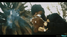 a man is smoking a cigarette in front of a palm tree and the word trilla is on the bottom right