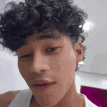 a man with curly hair and a white tank top looks at the camera