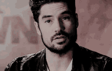 a man with a beard is wearing a leather jacket and a white shirt