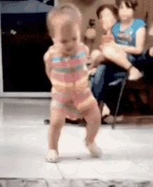 a little girl is dancing in a room while a woman holds another child