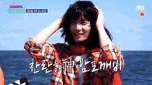 a woman in a plaid shirt is standing in front of the ocean