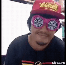 a man wearing a red hat and pink hypnotic glasses is smiling .