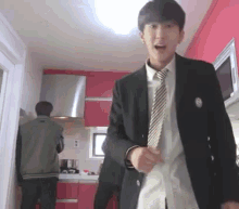 a man in a suit and tie is standing in a kitchen with a man standing behind him .