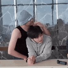 a man in a black tank top is hugging another man in a grey hoodie