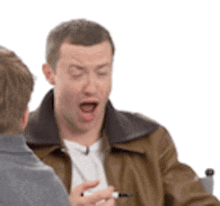 a man in a leather jacket is talking to another man in a chair .