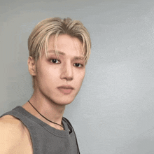 a man with blonde hair is wearing a grey tank top and a black necklace