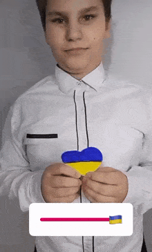 a boy in a white shirt is holding a blue and yellow heart in his hands