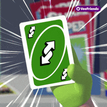 a hand is holding a green uno card with arrows on it