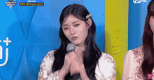 a girl in a white dress holds her hands together in front of a sign that says mnet