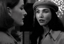 a woman wearing a beret and a trench coat talks to another woman