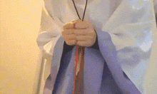 a person wearing a white robe and a purple skirt is holding a red object in their hands .