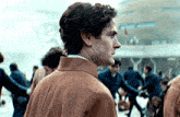 a man in a brown coat stands in front of a crowd