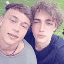 two young men with curly hair are posing for a picture together in the grass .
