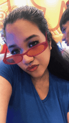a woman wearing red sunglasses and a blue shirt is taking a selfie