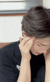 a man wearing a black t-shirt with the letter t on it touches his forehead