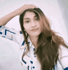 a woman with long hair is wearing a blue and white shirt and touching her head