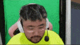 a man with a beard wearing headphones and a microphone is sitting in front of a green screen .