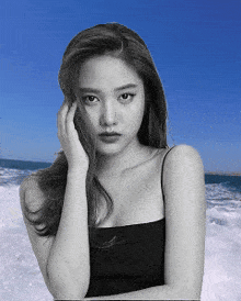 a woman in a black tank top stands in front of a beach