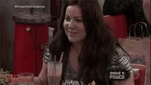 a woman sits at a table with a drink in front of a sign that says programa da sabrina