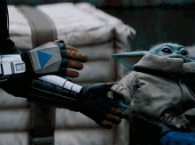 a baby yoda is being held by a person with a triangle on their glove