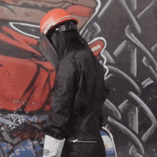 a person wearing a hard hat and a face shield is standing in front of a graffiti wall