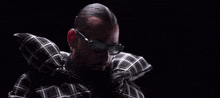 a man with a beard and sunglasses is wearing a plaid shirt and a pillow around his neck .