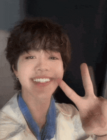 a young man with short hair is smiling and making a peace sign