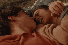 a man and a woman are kissing while laying on a picnic blanket .