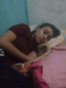 a woman in a maroon shirt is laying on a bed with a pink blanket