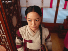 a woman in a traditional korean dress stands in front of a window with drxx_yxh written in the corner