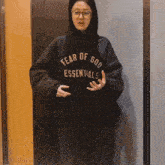 a woman wearing a fear of god essentials hoodie