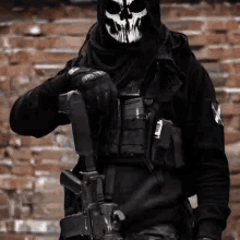 a soldier with a skull mask on his face is holding a gun in front of a brick wall .